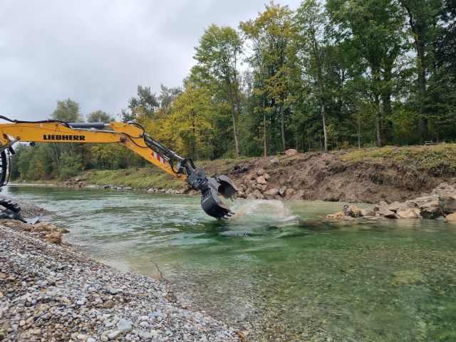 Der Bagger baut die Wasserbausteine aus der Uferbestigung als Buhne ein, so dass die Entwicklung der Ufers beschleunigt wird Der Bagger baut die Wasserbausteine aus der Uferbestigung als Buhne ein, so dass die Entwicklung der Ufers beschleunigt wird